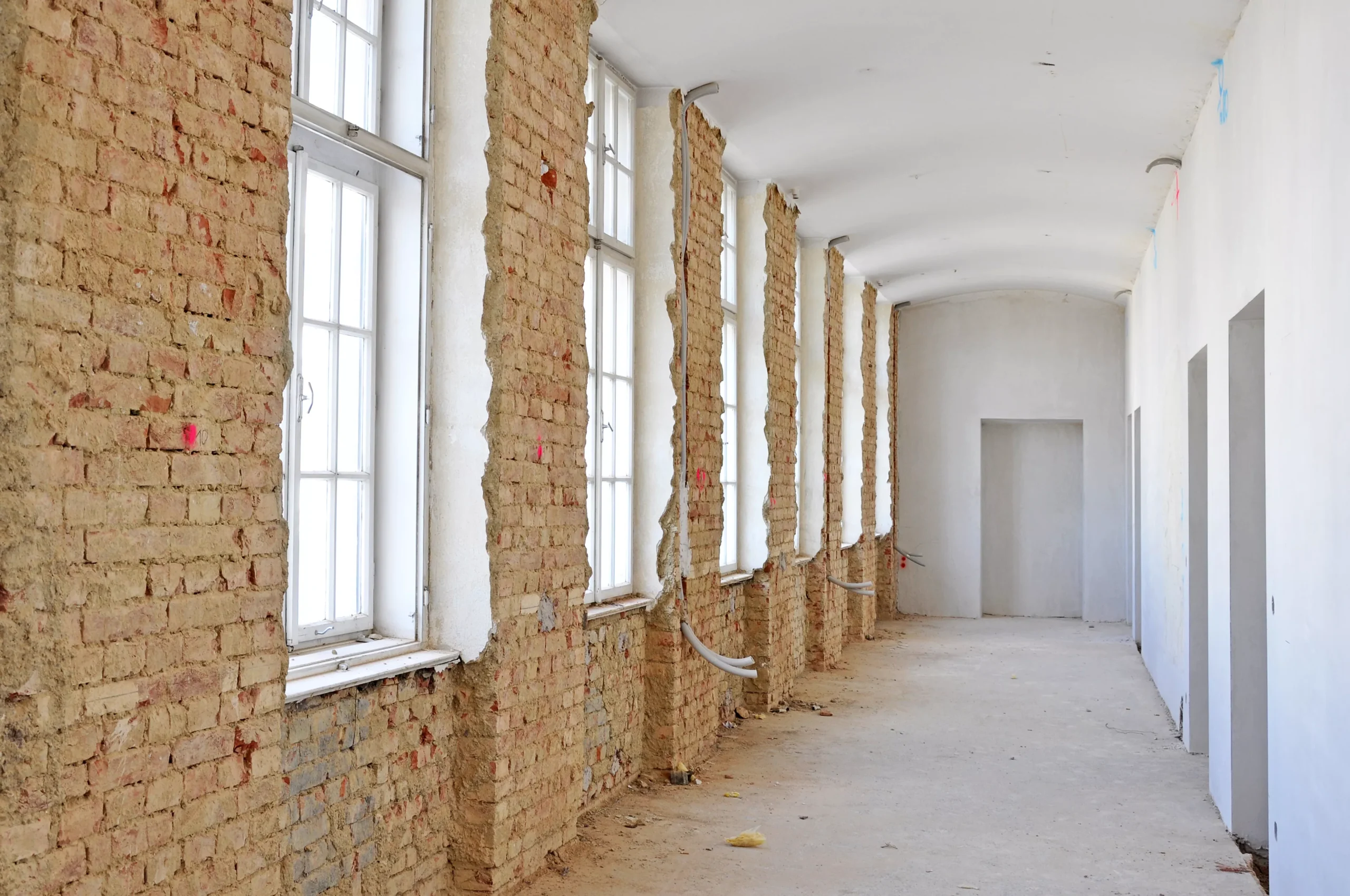 Entkernter Altbau mit freigelegtem Ziegelmauerwerk und hohen Fenstern vor der Sanierung